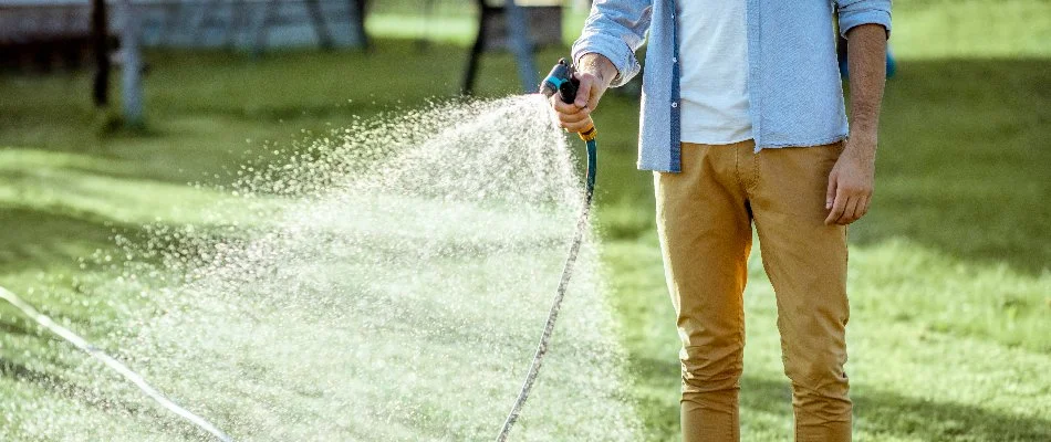 Man watering a lawn in Matthews, NC, using a hose sprayer.